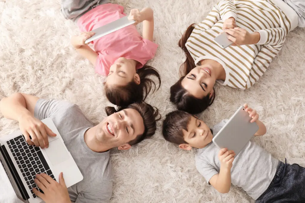 Xfinity Mobile customers in Illinois enjoy fast WiFi on their devices on the Premium Unlimited plan. IMAGE: Family of four on a carpeted floor each enjoying wifi access on different devices.