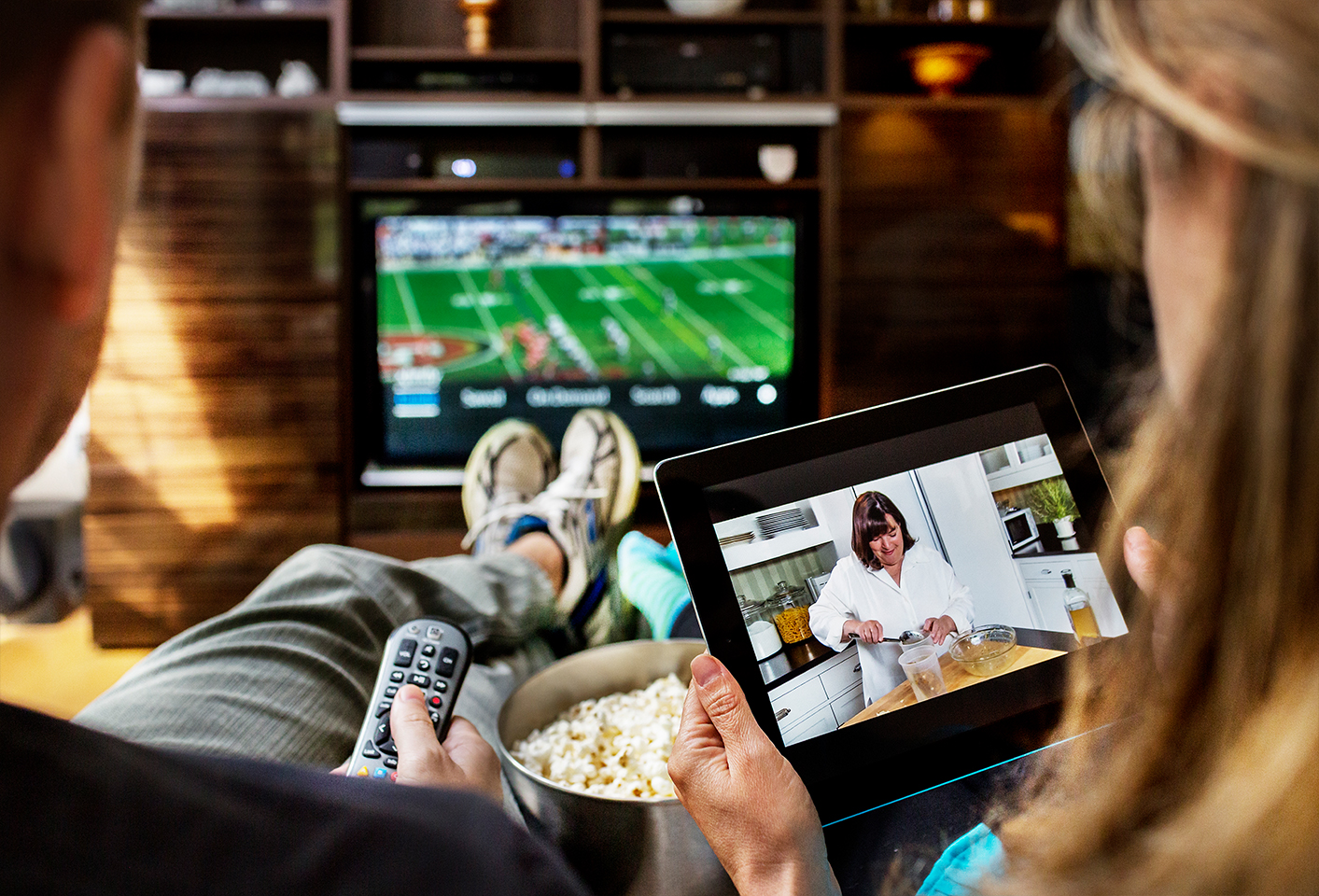 Two people sitting on a couch watching television on a tablet and on a TV.