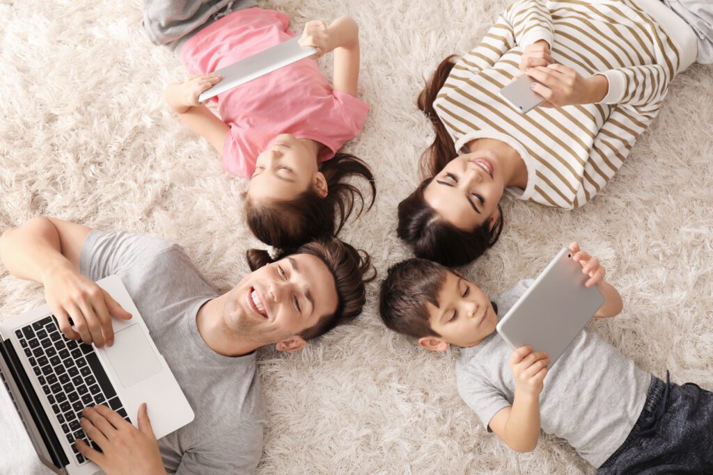 Xfinity Mobile customers in Illinois enjoy fast WiFi on their devices on the Premium Unlimited plan. IMAGE: Family of four on a carpeted floor each enjoying wifi access on different devices.